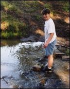 Boy in white t-shirt and shorts next to a stream