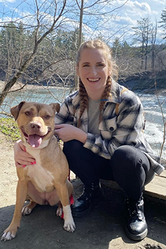 woman in front of a river smiling at the camera with a dog