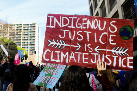 Red sign with text 'Indigenous Justice is Climate Justice' being held up during march