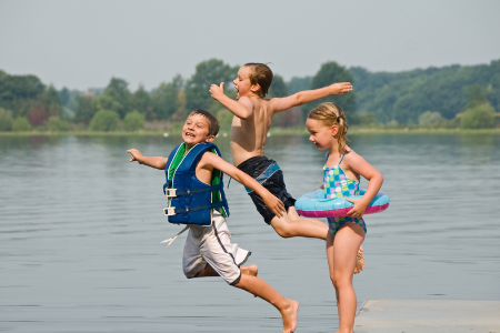 Kids in swimsuits and life jackets jumping into lake