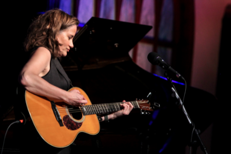 Susan Werner plays acoustic guitar in front of grand piano